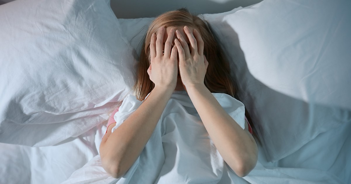 Mujer en la cama con manos sobre la cara experimentando insomnio por ansiedad