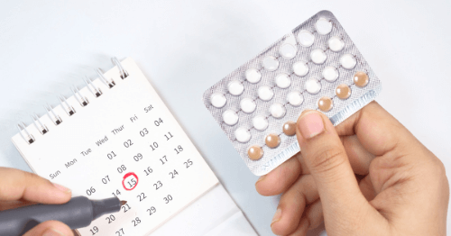 Manos de mujer sujetando un blíster de anticonceptivas y un calendario