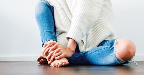 Mujer sentada en el suelo con dolor articular, uno de los síntomas físicos de la menopausia.