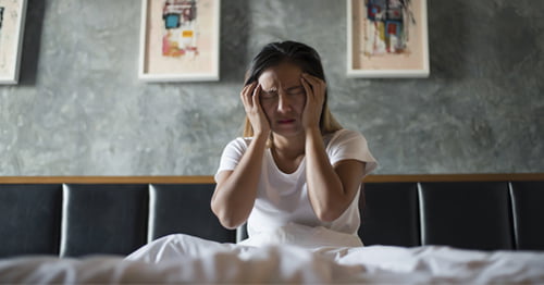 Mujer acostada en la cama con dolor de cabeza por culpa de la menopausia.