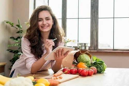 Mujer contenta haciendo lista con comida saludable