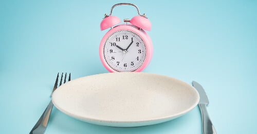 Un plato vacío y un reloj representando el concepto de ayuno intermitente en la menopausia