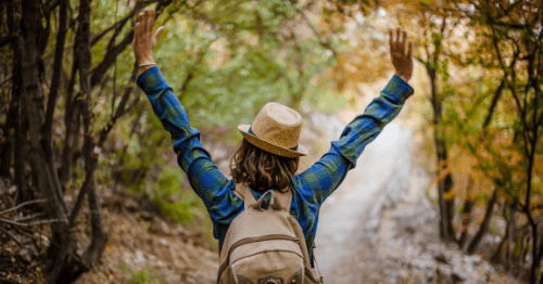 Mujer con mochila de espaldas en un bosque levantando los brazos