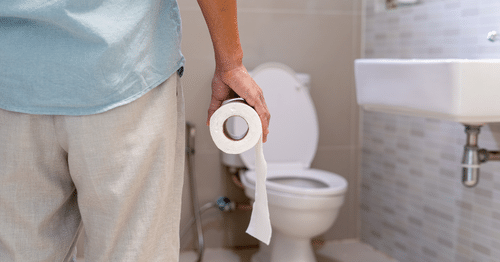Hombre de espaldas en el baño sujetando un rollo de papel higiénico