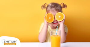Niña sosteniendo dos naranjas en la cara y tomando un zumo para subir las defensas