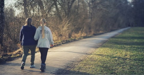Dos amigas de espaldas caminando, uno de los ejercicios buenos para bajar el colesterol