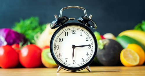 Reloj sobre una mesa con frutas y vegetales al fondo