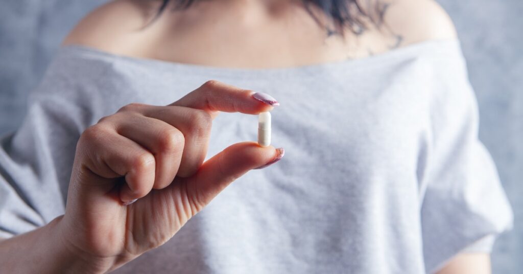 Imagen de cabecera del artículo sobre las contraindicaciones de pcos niam. Mujer sosteniendo una cápsula de un suplemento natural