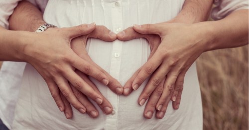 Mujer embarazada con sus manos y las de su pareja sobre la barriga formando un corazón