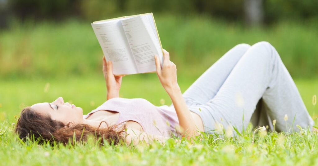 Mujer leyendo tumbada en el campo, una de las formas de aliviar el estrés emocional