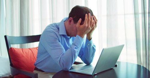 Hombre sentado ante un ordenador con las manos sobre el rostro con estrés emocional